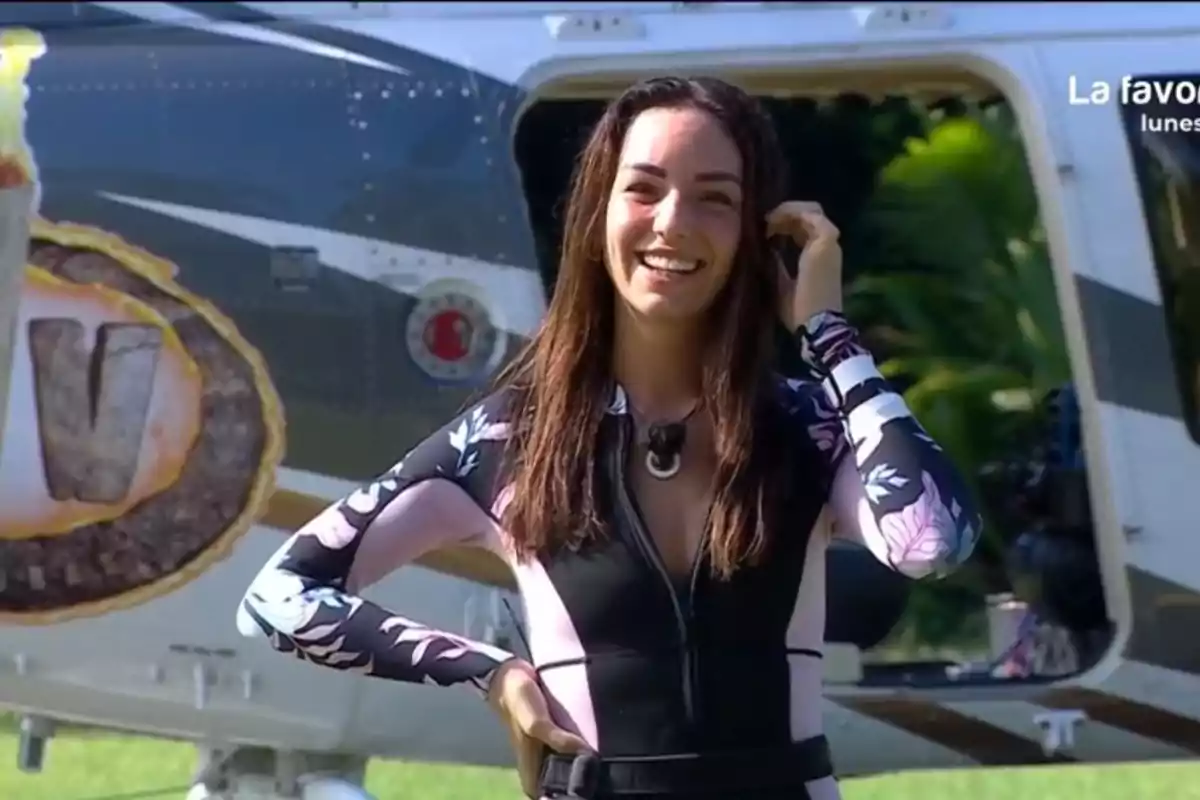 Anita sonriente con un traje de neopreno floral está de pie frente a un helicóptero en un entorno al aire libre. Anita sonriente con un traje de neopreno floral está de pie frente a un helicóptero en un entorno al aire libre.