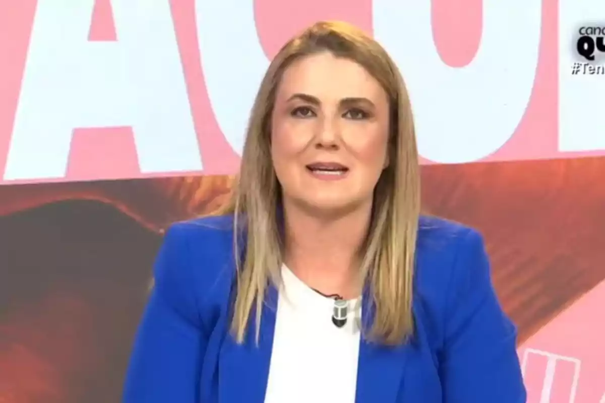 Una persona amb cabell ros i jaqueta blava apareix en un programa de televisió amb un fons acolorit. Una persona amb cabell ros i jaqueta blava apareix en un programa de televisió amb un fons acolorit.