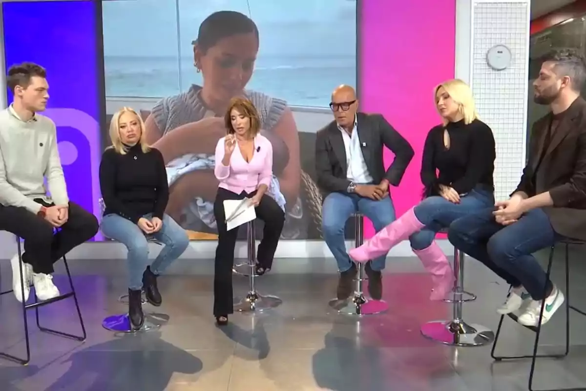 Un grup de persones assegudes en tamborets en un plató de televisió amb una pantalla gran de fons mostrant una dona sostenint un nadó.