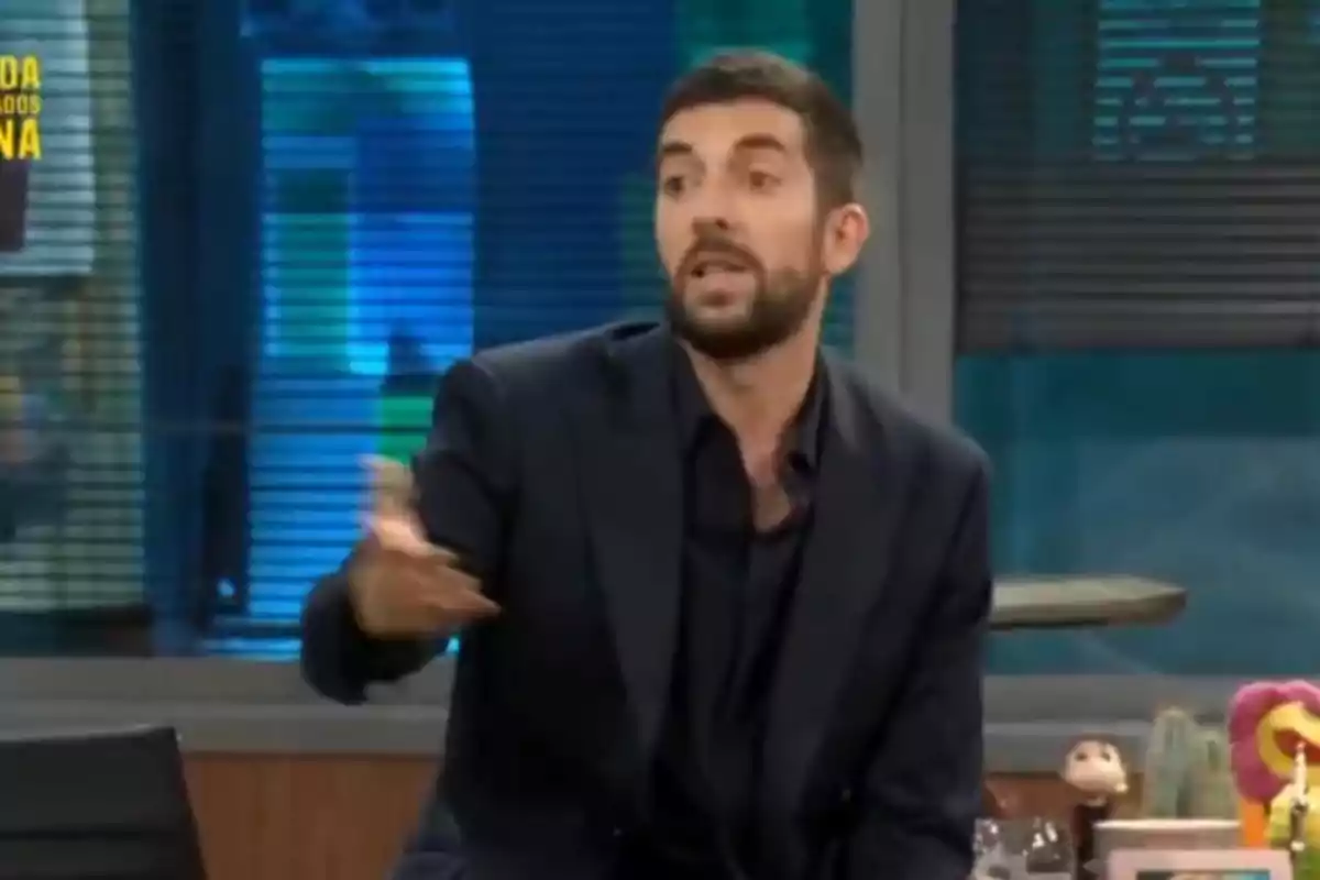 David Broncano con barba y traje oscuro gesticula mientras habla en un programa de televisión. David Broncano con barba y traje oscuro gesticula mientras habla en un programa de televisión.