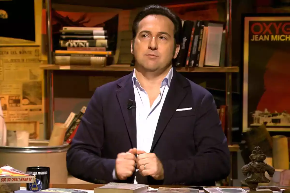 Iker Jiménez de pie en un estudio rodeado de libros y objetos decorativos.