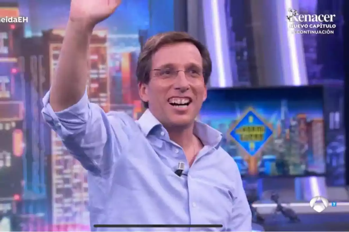 José Luis Martínez-Almeida con camisa azul sonríe y saluda en un set de televisión colorido. José Luis Martínez-Almeida con camisa azul sonríe y saluda en un set de televisión colorido.