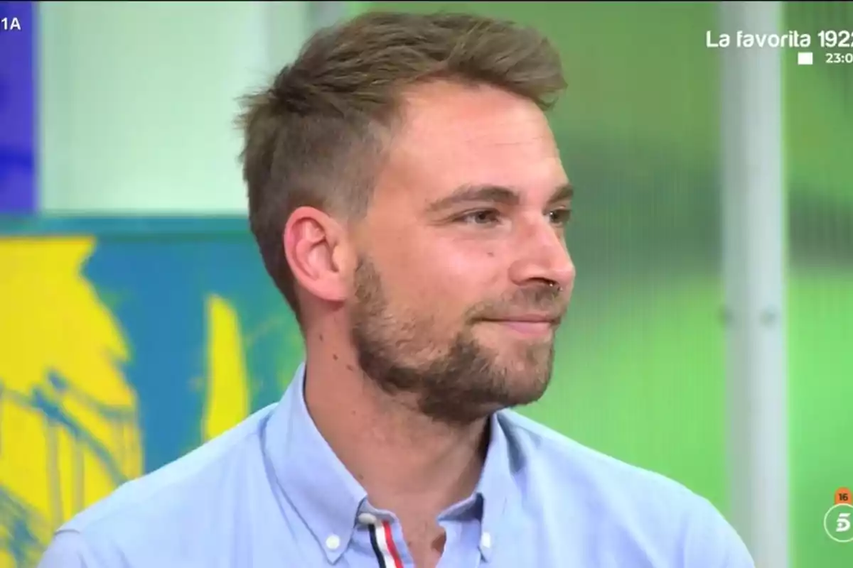 Un home amb barba i cabell curt porta una camisa blau clar mentre somriu lleugerament en un entorn interior amb fons acolorit. Un home amb barba i cabell curt porta una camisa blau clar mentre somriu lleugerament en un entorn interior amb fons acolorit.