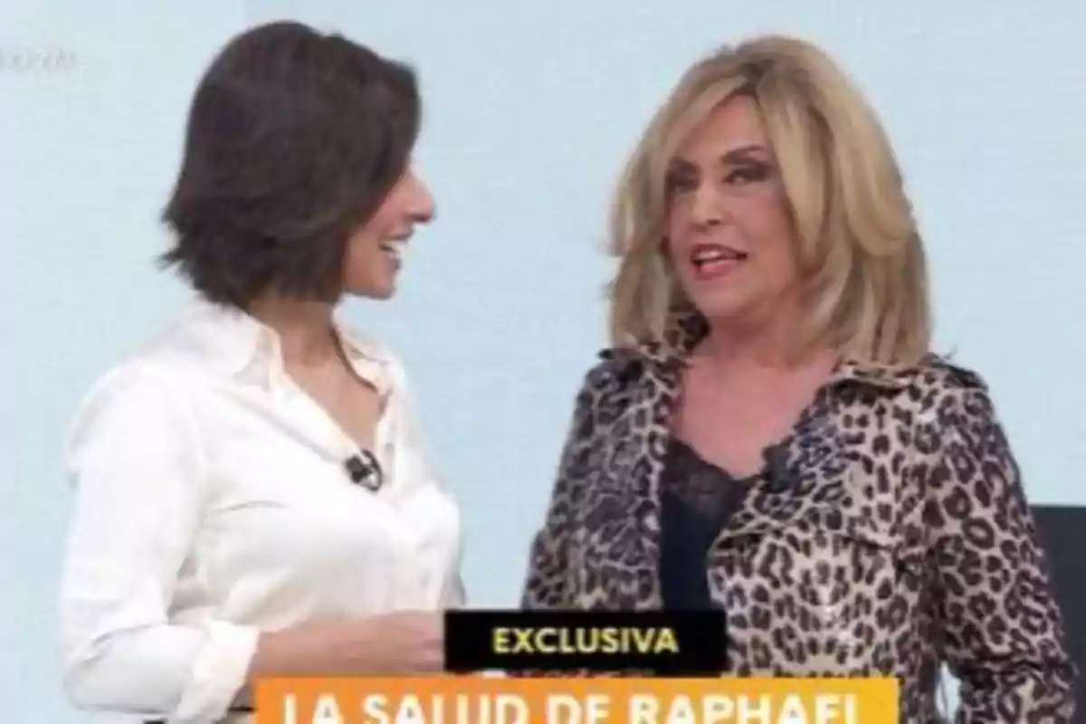Lydia Lozano y Adela González conversando en un programa de televisión, una con camisa blanca y otra con chaqueta de estampado animal, con un texto en la parte inferior que dice Lydia Lozano y Adela González conversando en un programa de televisión, una con camisa blanca y otra con chaqueta de estampado animal, con un texto en la parte inferior que dice