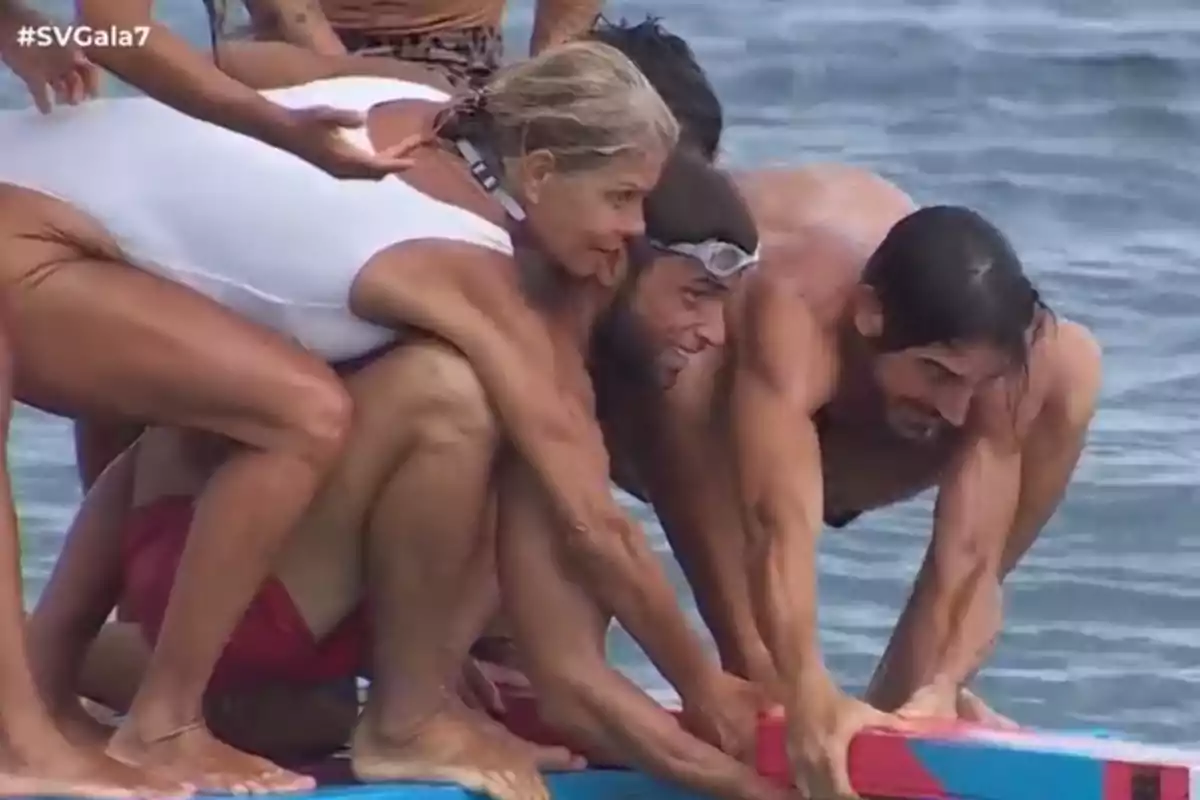 Un grupo de personas en traje de baño se agacha sobre una tabla en el agua, participando en una actividad o desafío. Un grupo de personas en traje de baño se agacha sobre una tabla en el agua, participando en una actividad o desafío.