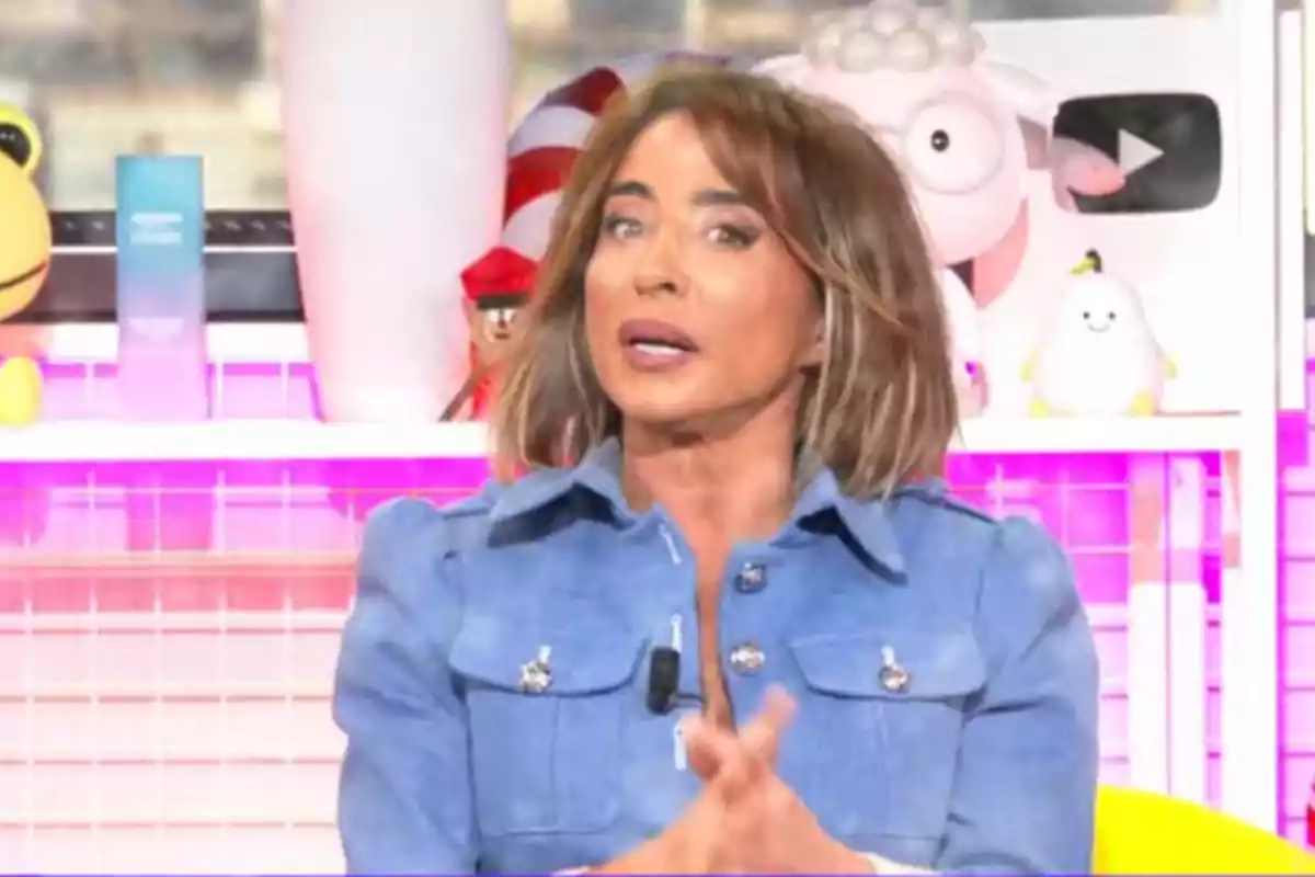 María Patiño con chaqueta azul en un set de televisión colorido con juguetes y decoraciones en el fondo. María Patiño con chaqueta azul en un set de televisión colorido con juguetes y decoraciones en el fondo.