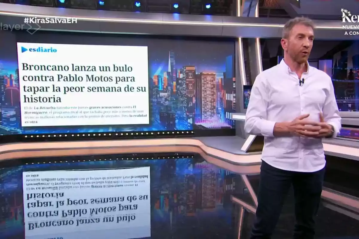 Un home dret en un set de televisió al costat d?una pantalla que mostra un titular de notícies. Un home dret en un set de televisió al costat d?una pantalla que mostra un titular de notícies.