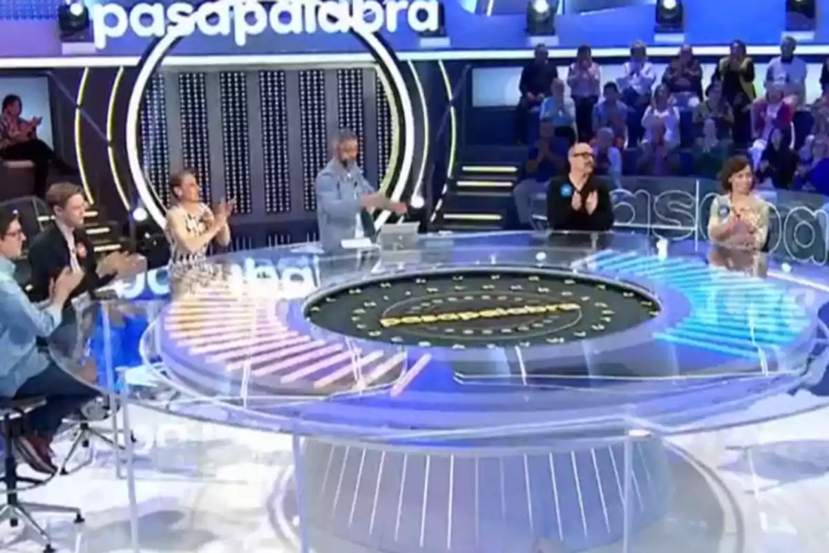Un grup de persones aplaudeix en un plató de televisió amb un disseny circular i un públic al fons.