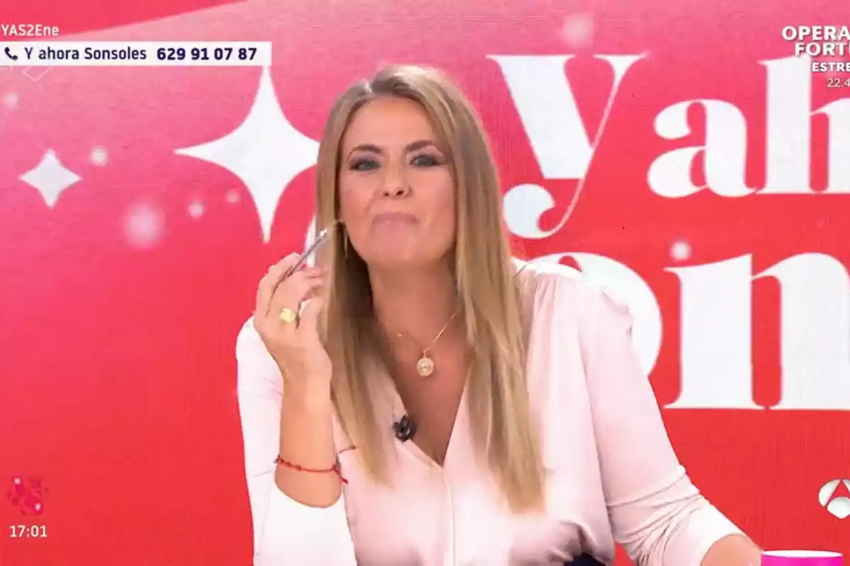 Pepa Romero con cabello rubio y blusa clara sostiene un bolígrafo frente a un fondo rojo con texto blanco. Pepa Romero con cabello rubio y blusa clara sostiene un bolígrafo frente a un fondo rojo con texto blanco.