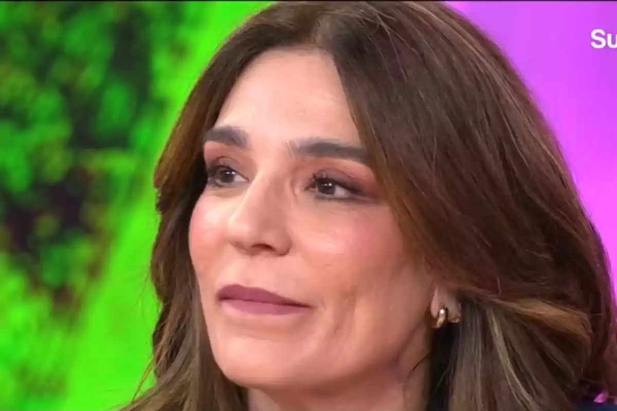 Raquel Bollo con cabello castaño y maquillaje sutil mira hacia un lado con una expresión serena mientras el fondo muestra colores vibrantes.