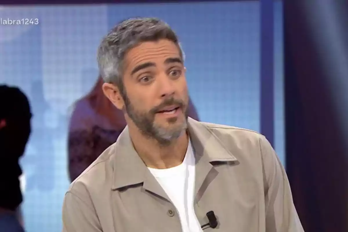 Un home amb barba i cabell canós està parlant en un programa de televisió, porta una jaqueta beix i una samarreta blanca. Un home amb barba i cabell canós està parlant en un programa de televisió, porta una jaqueta beix i una samarreta blanca.