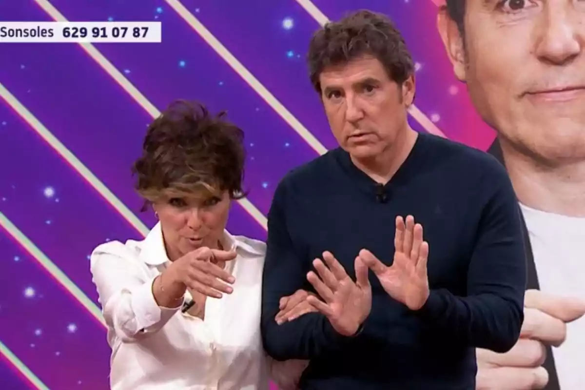 Dues persones en un plató de televisió amb un fons acolorit i un número de telèfon visible a la cantonada superior esquerra. Dues persones en un plató de televisió amb un fons acolorit i un número de telèfon visible a la cantonada superior esquerra.