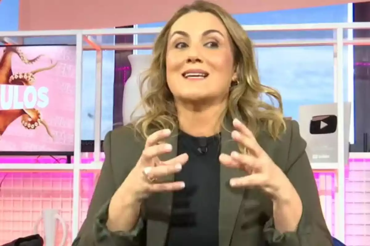 Una persona gesticulant amb les mans mentre parla en un plató de televisió amb una pantalla i un trofeu de YouTube al fons. Una persona gesticulant amb les mans mentre parla en un plató de televisió amb una pantalla i un trofeu de YouTube al fons.
