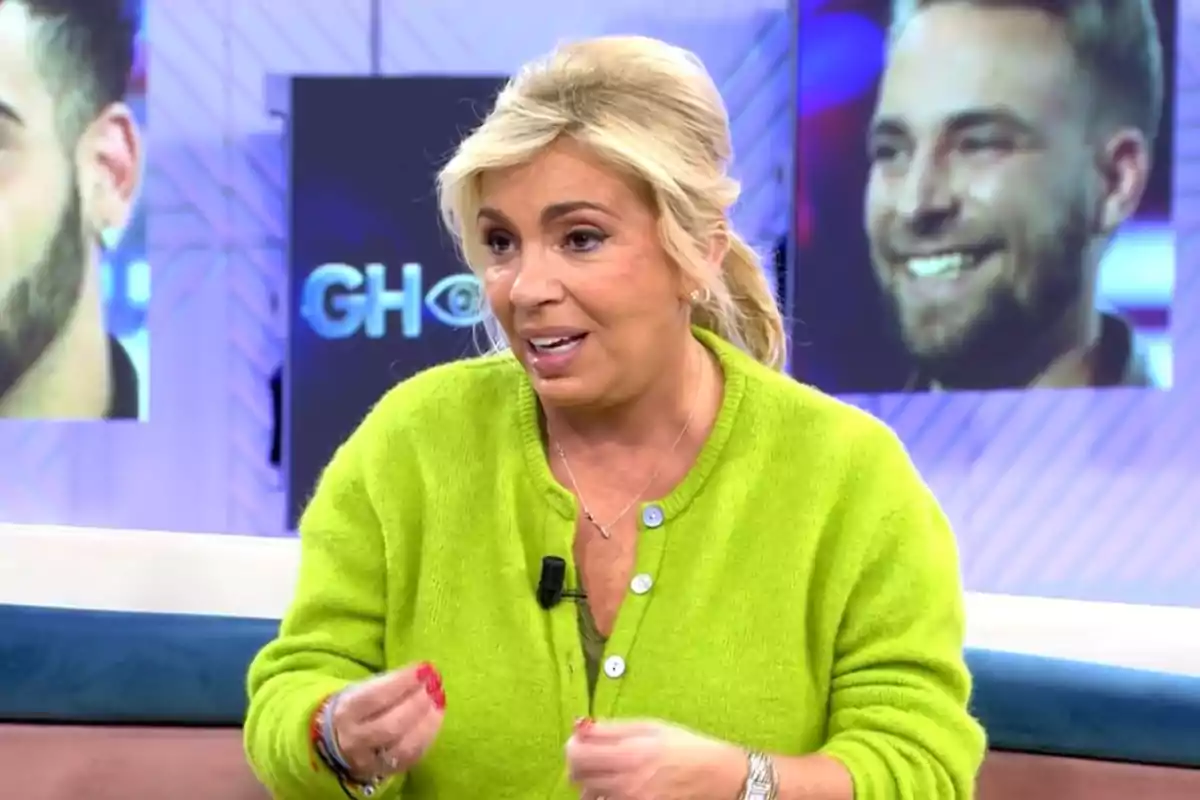 Una dona amb suèter verd parlant en un set de televisió amb pantalles al fons.