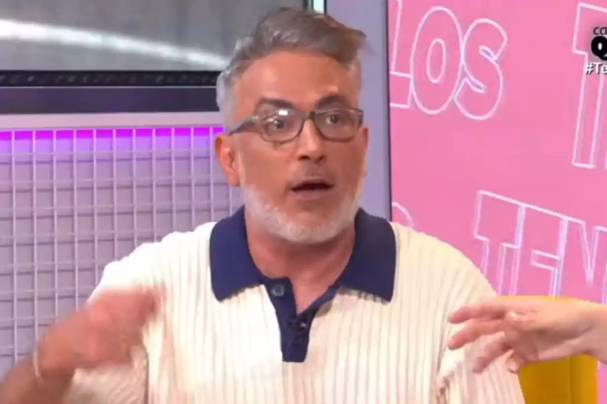 Un home amb ulleres i barba canosa està parlant en un programa de televisió amb un fons rosa i lletres blanques.