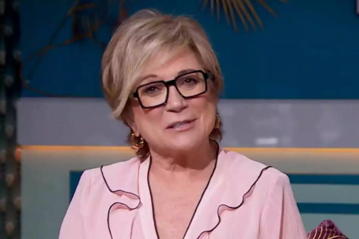 Inés Ballester con gafas y cabello corto rubio, vistiendo una blusa rosa, está sonriendo frente a un fondo azul en Cine de Barrio. Inés Ballester con gafas y cabello corto rubio, vistiendo una blusa rosa, está sonriendo frente a un fondo azul en Cine de Barrio.