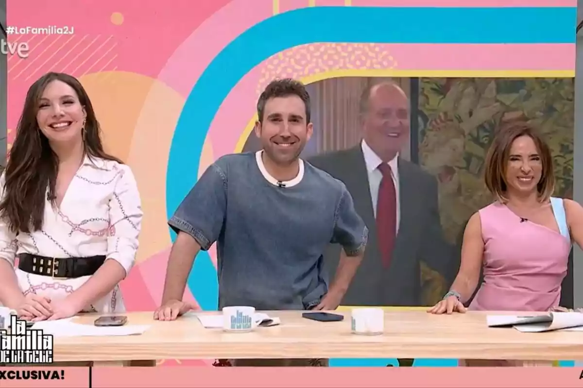 Inés Hernand, Aitor Albizua i María Patiño somriuen en un plató de televisió de La Família de la Tele acolorit amb una pantalla al fons que mostra un home gran elegantment vestit.