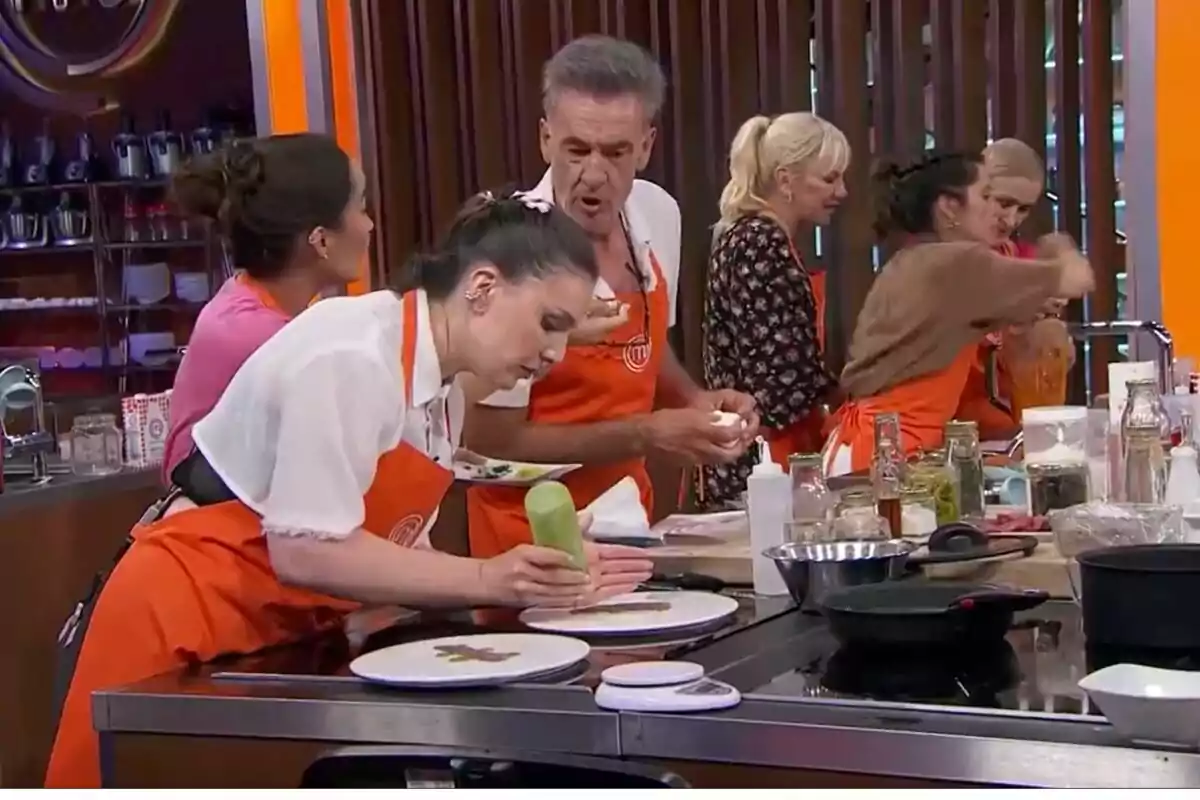 Persones com Inés Hernand, Francis Lorenzo, María León, Topacio Fresh o Cristina Cifuentes cuinant en una competència culinària, usant davantals taronges i concentrades en els seus plats a MasterChef Celebrity. Persones com Inés Hernand, Francis Lorenzo, María León, Topacio Fresh o Cristina Cifuentes cuinant en una competència culinària, usant davantals taronges i concentrades en els seus plats a MasterChef Celebrity.