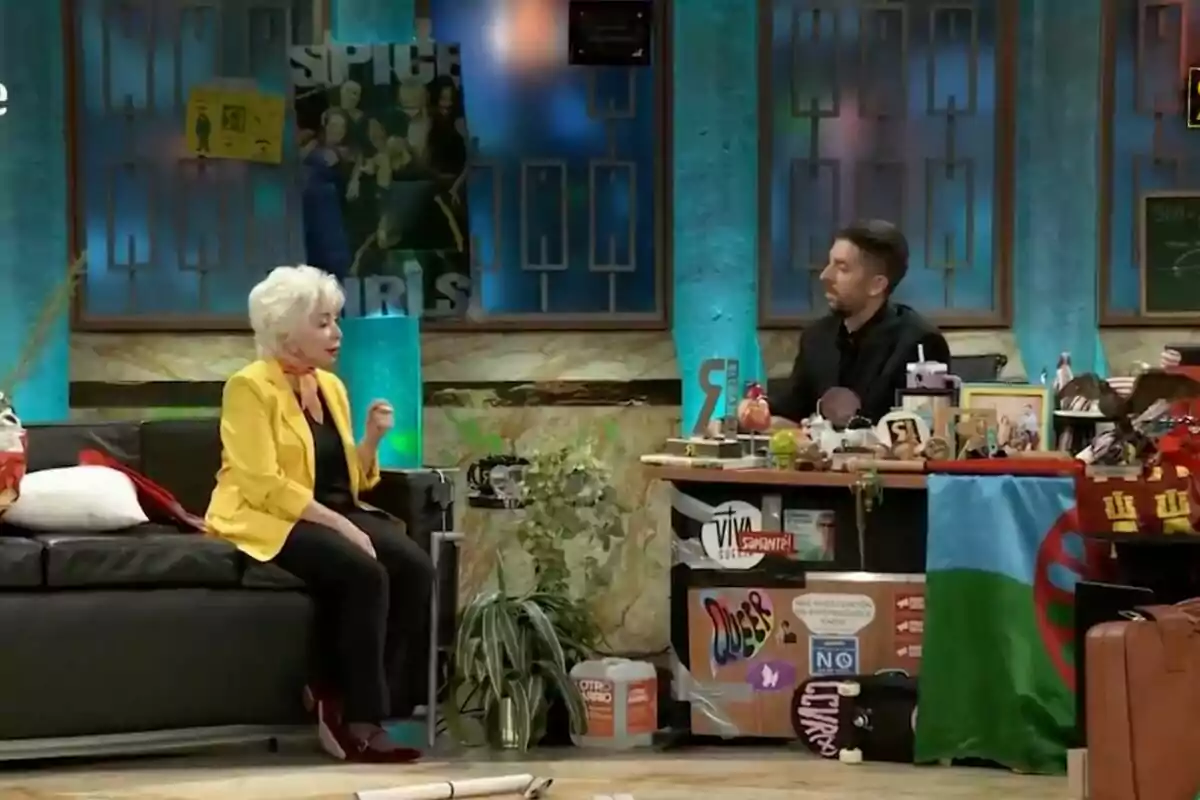 Isabel Allende con cabello blanco y chaqueta amarilla está sentada en un sofá negro, conversando con David Broncano detrás de un escritorio lleno de objetos decorativos en 'La Revuelta'. Isabel Allende con cabello blanco y chaqueta amarilla está sentada en un sofá negro, conversando con David Broncano detrás de un escritorio lleno de objetos decorativos en 'La Revuelta'.