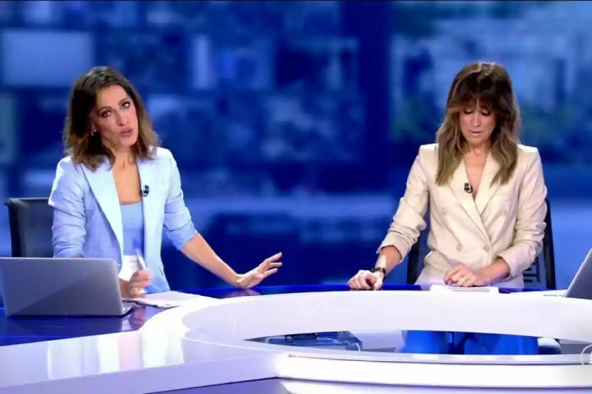 Isabel Jiménez emocionada junto a Ángeles Blanco sentadas en el plató de Informativos Telecinco con ordenadores portátiles frente a ellas. Isabel Jiménez emocionada junto a Ángeles Blanco sentadas en el plató de Informativos Telecinco con ordenadores portátiles frente a ellas.
