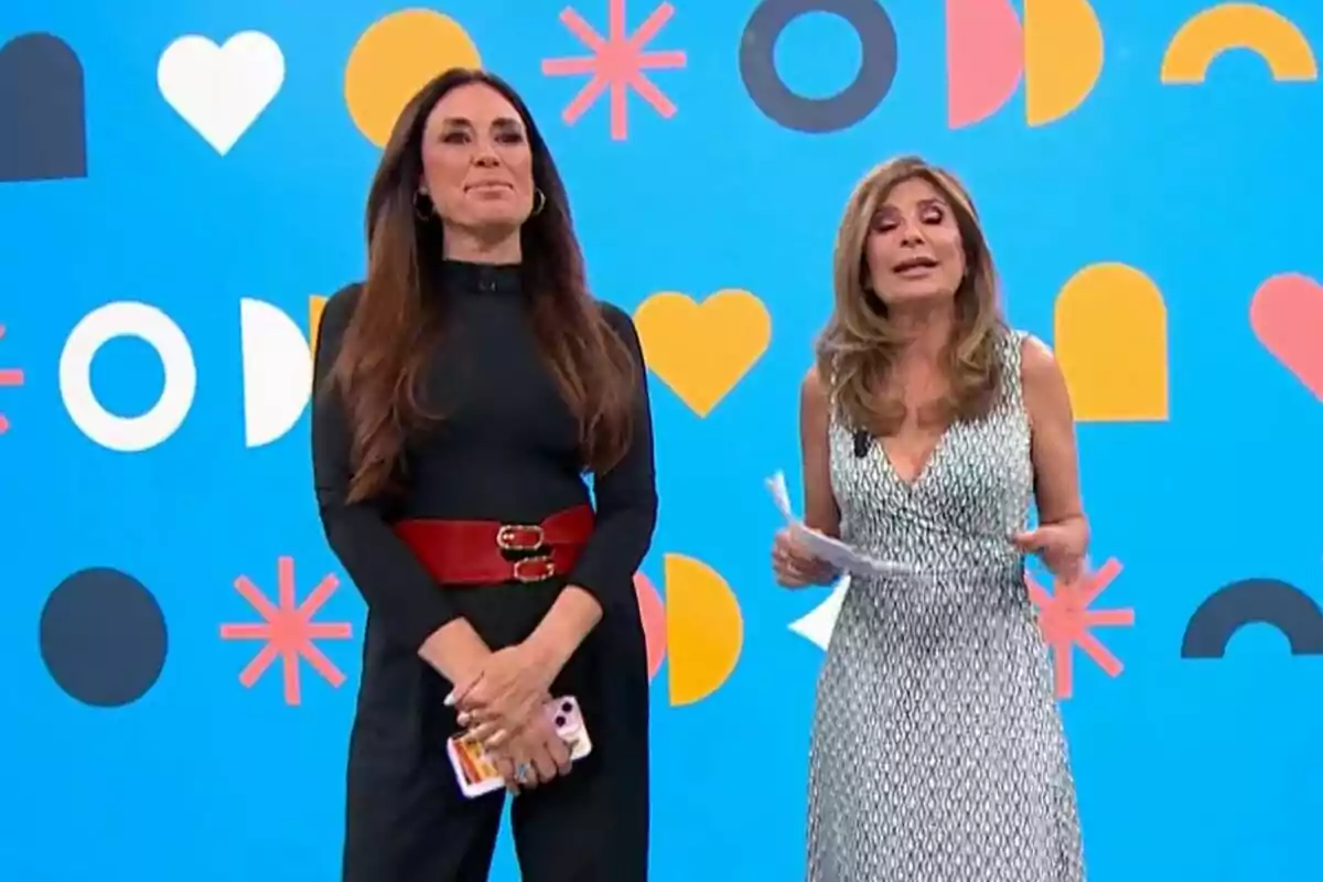 Isabel Rábago y Gema López de pie en Espejo Público con un fondo azul decorado con formas geométricas y corazones una lleva un vestido negro con un cinturón rojo y la otra un vestido blanco y negro. Isabel Rábago y Gema López de pie en Espejo Público con un fondo azul decorado con formas geométricas y corazones una lleva un vestido negro con un cinturón rojo y la otra un vestido blanco y negro.