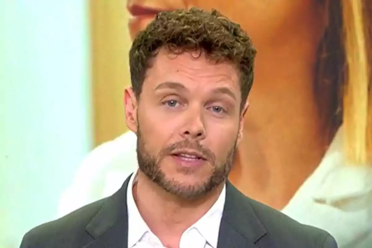 Jano Mecha con barba y cabello rizado lleva un traje oscuro y camisa blanca mientras habla frente a un fondo desenfocado en El Programa de Ana Rosa.
