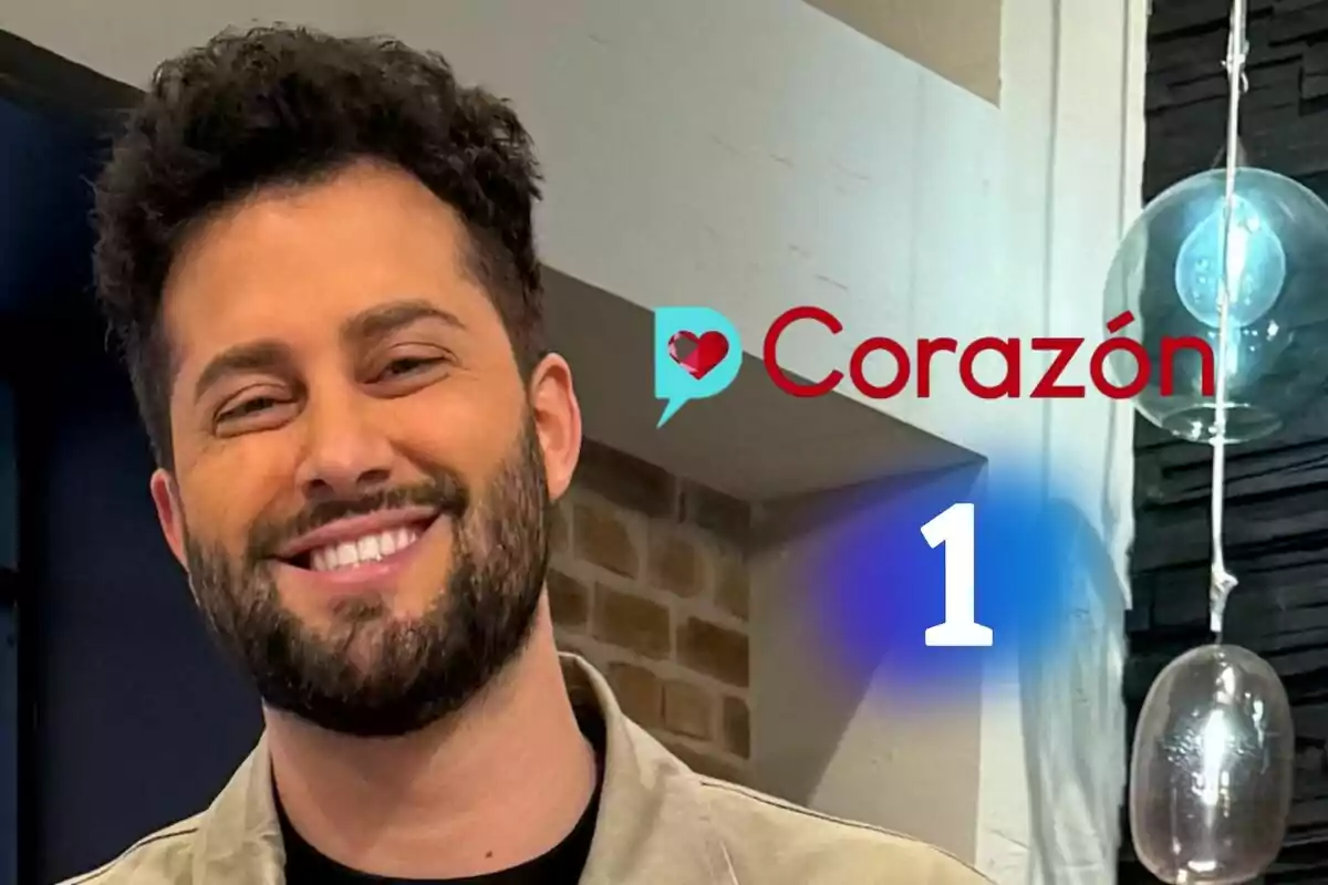 Javi de Hoyos sonriente con barba y cabello rizado en un estudio con el logo de D Corazón y el logo de La 1 al fondo