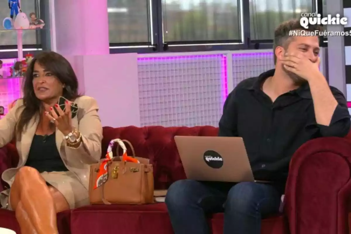 Dos personas sentadas en un sofá rojo, Aida Nízar con un bolso marrón y Javi de Hoyos con una computadora portátil, en un set de televisión con el logo de Dos personas sentadas en un sofá rojo, Aida Nízar con un bolso marrón y Javi de Hoyos con una computadora portátil, en un set de televisión con el logo de