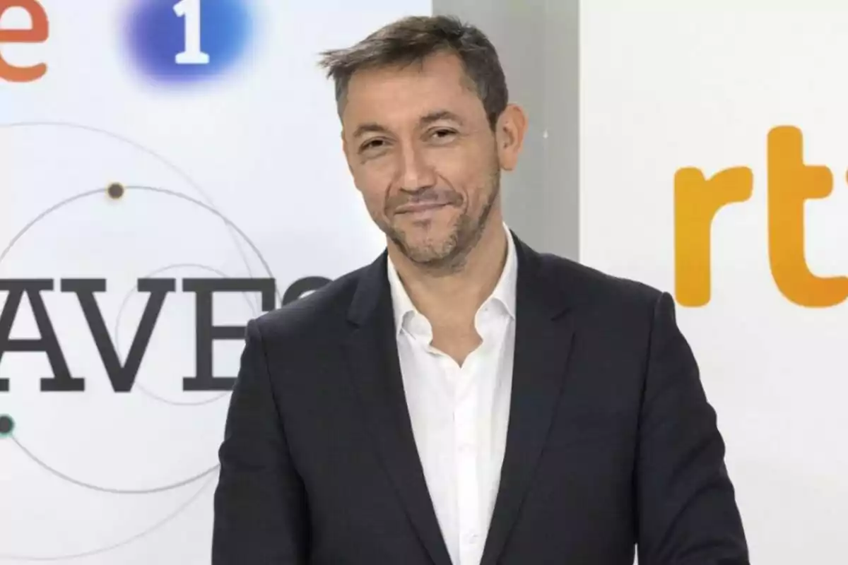 Javier Ruiz con traje oscuro y camisa blanca sonríe frente a un fondo con logotipos y letras. Javier Ruiz con traje oscuro y camisa blanca sonríe frente a un fondo con logotipos y letras.