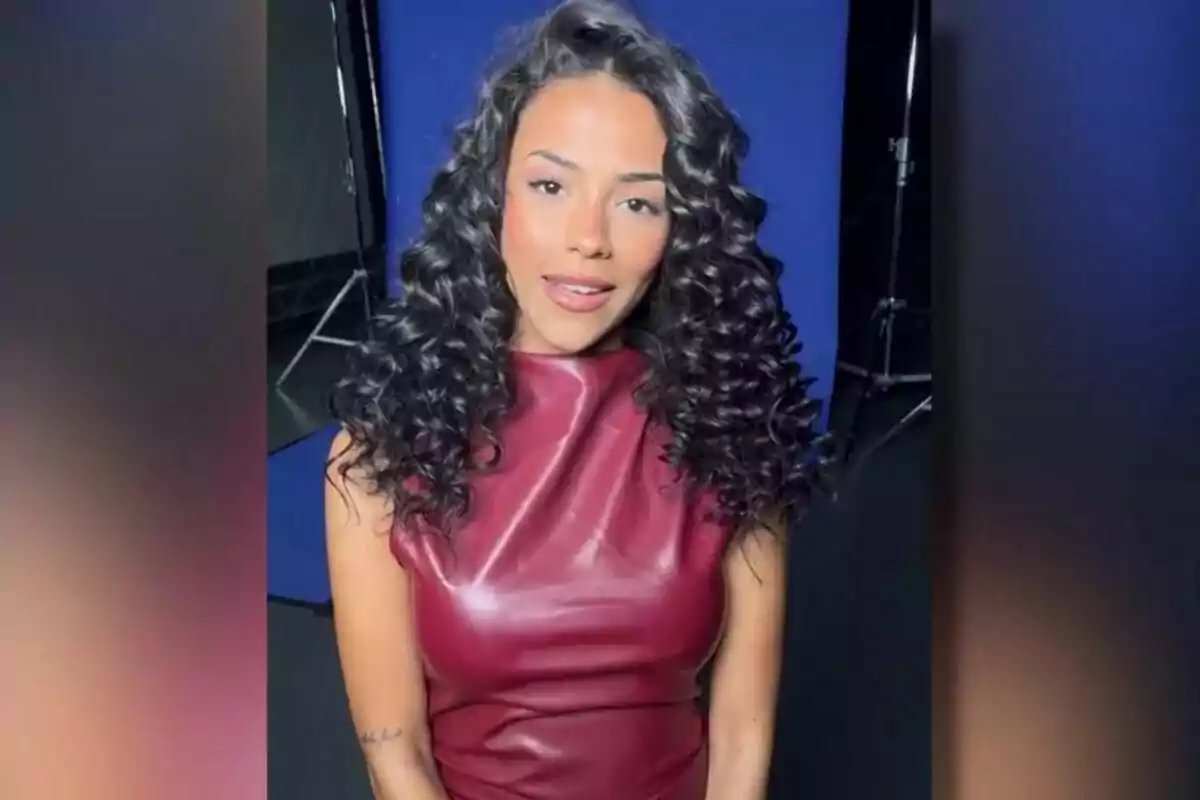 Jeimy Báez amb cabell arrissat i llarg porta un vestit de cuir vermell fosc, posant davant d'un fons blau en un estudi fotogràfic a GH DÚO. Jeimy Báez amb cabell arrissat i llarg porta un vestit de cuir vermell fosc, posant davant d'un fons blau en un estudi fotogràfic a GH DÚO.