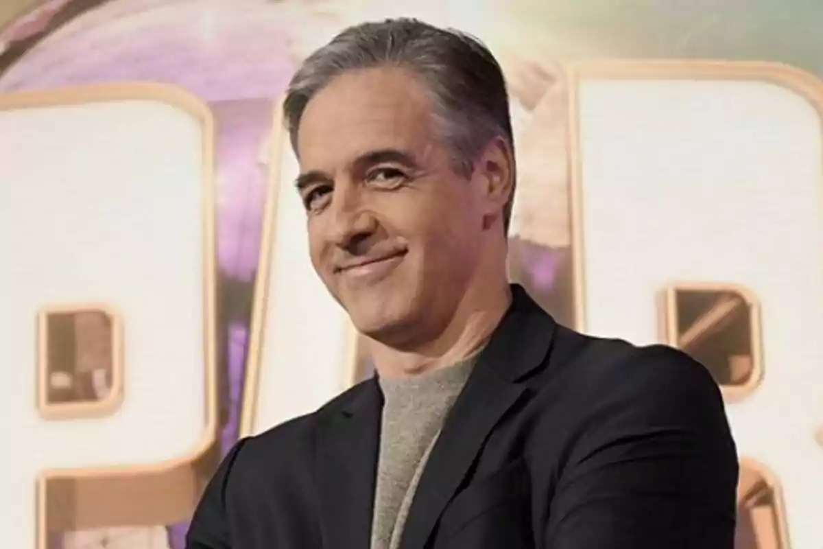Paco de Benito de cabello canoso sonriendo con fondo de letras grandes de Jeopardy!
