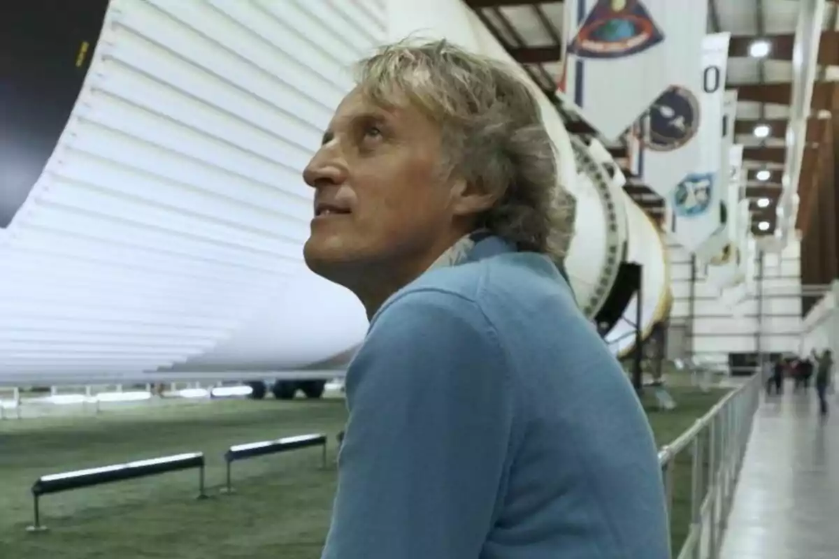 Jesús Calleja de cabello canoso y suéter azul observa un cohete en un museo aeroespacial en Calleja en el espacio.