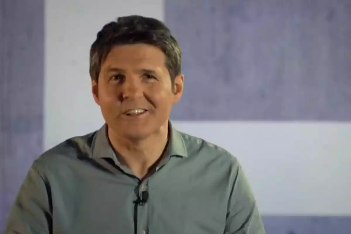 Jesús Cintora con camisa azul claro y micrófono de solapa sonríe frente a un fondo gris en Malas Lenguas.