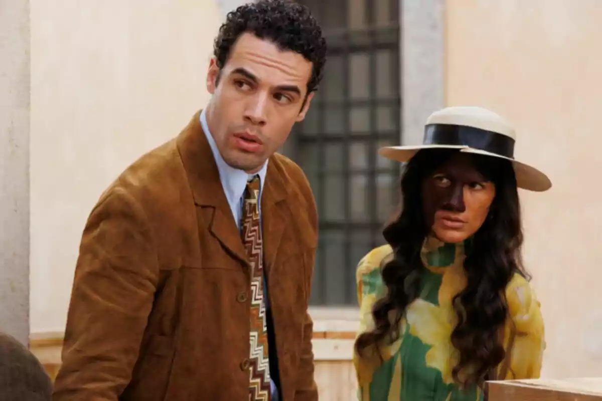 Jesús Mosquera con otra mujer con expresiones serias, una de ellas lleva un sombrero y un vestido colorido, mientras que la otra viste una chaqueta marrón y corbata estampada en La Moderna. Jesús Mosquera con otra mujer con expresiones serias, una de ellas lleva un sombrero y un vestido colorido, mientras que la otra viste una chaqueta marrón y corbata estampada en La Moderna.