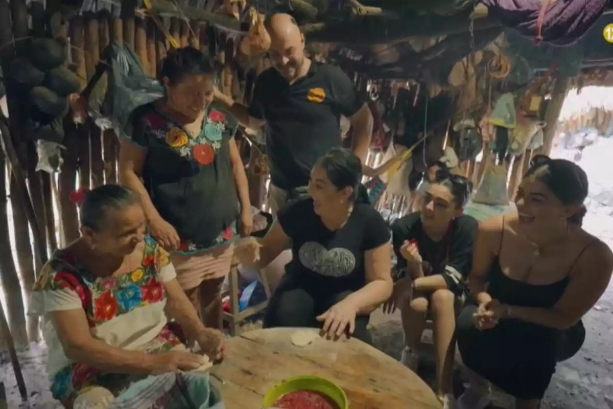 Los Jiménez sonríen y conversa mientras una mujer mayor prepara tortillas en una mesa dentro de una cabaña rústica en México en el programa de los 'Gipsy Kings.'
