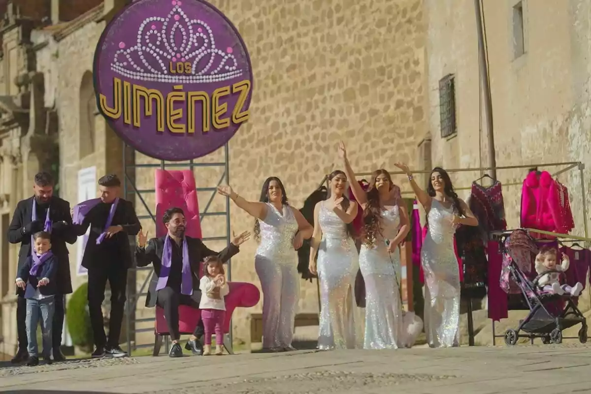 Un grupo de personas vestidas elegantemente posa frente a un cartel que dice 