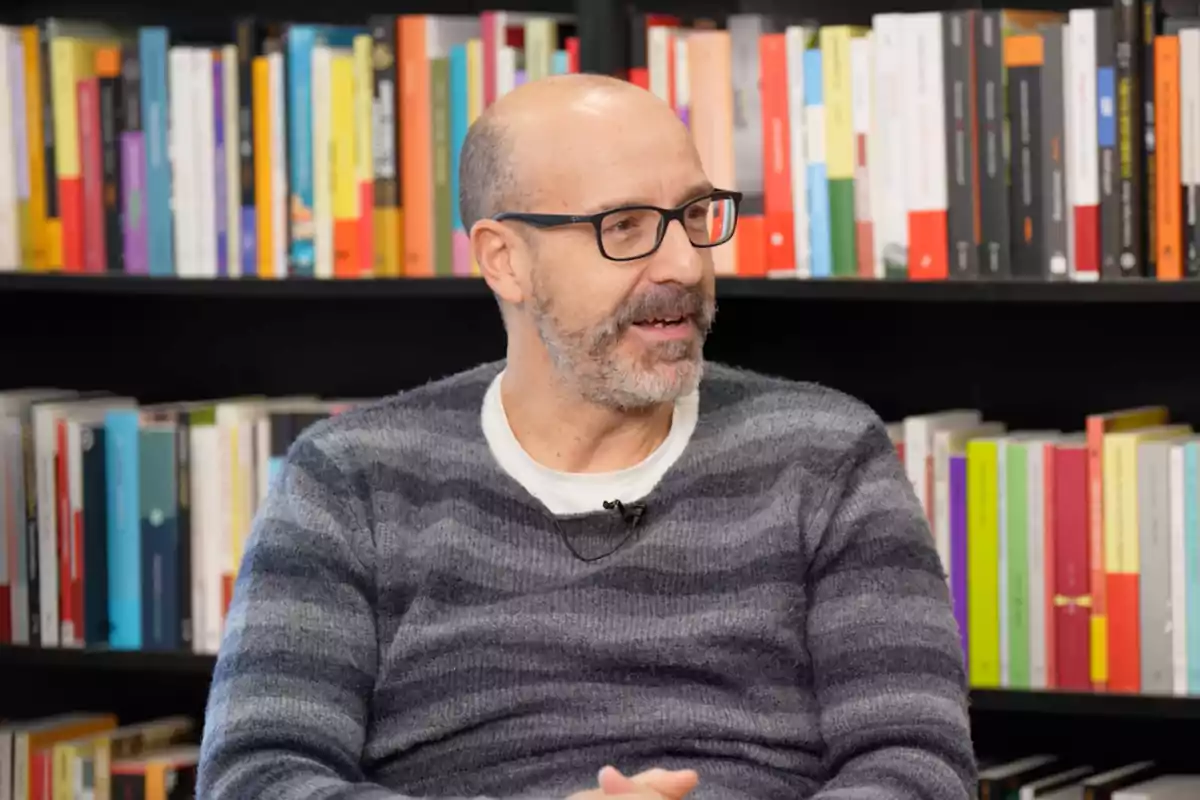 El periodista Joan María Pou assegut davant d'una prestatgeria plena de llibres.