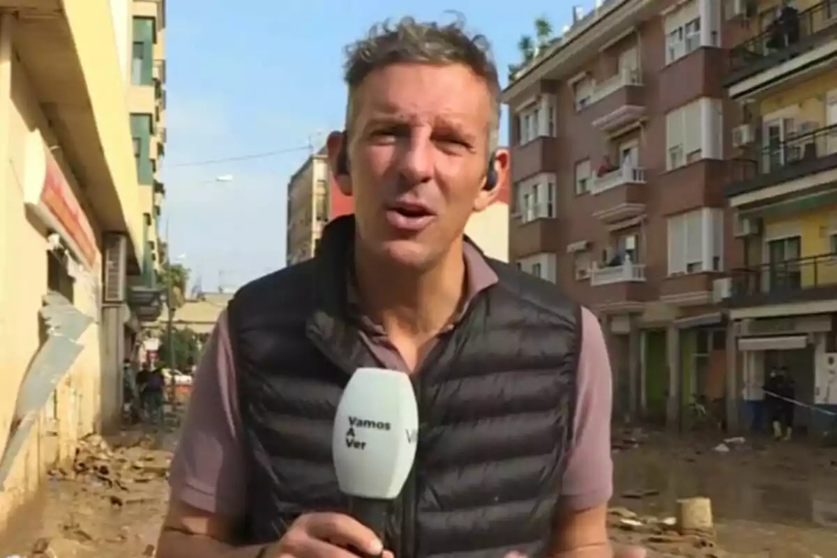 Joaquín Prat con chaleco negro sostiene un micrófono de Vamos a ver mientras informa desde una calle con edificios y escombros. Joaquín Prat con chaleco negro sostiene un micrófono de Vamos a ver mientras informa desde una calle con edificios y escombros.