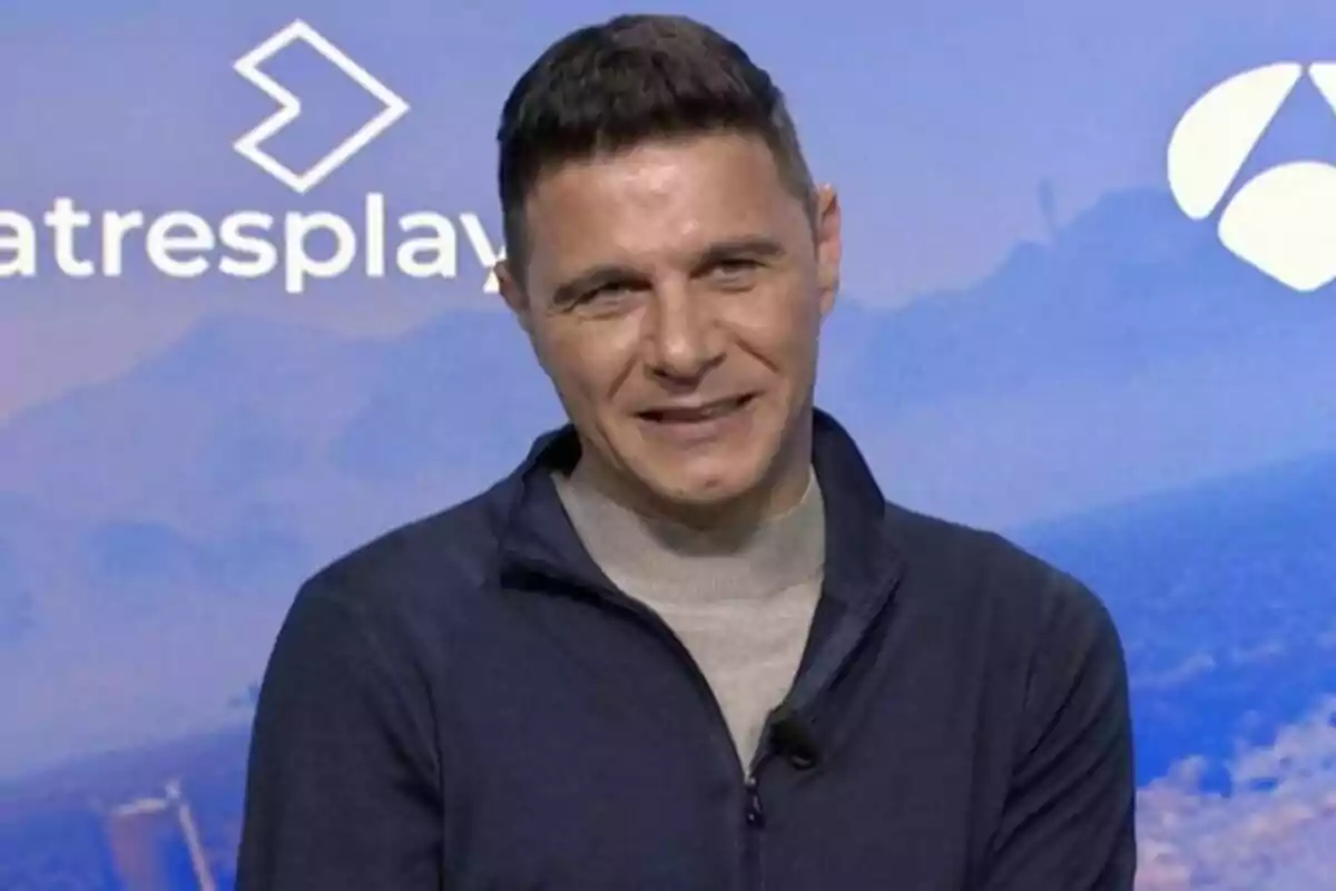 Joaquín Sánchez amb cabells curts i jaqueta fosca somriu davant d'un fons blau amb logotips a la presentació del Capità a Amèrica.
