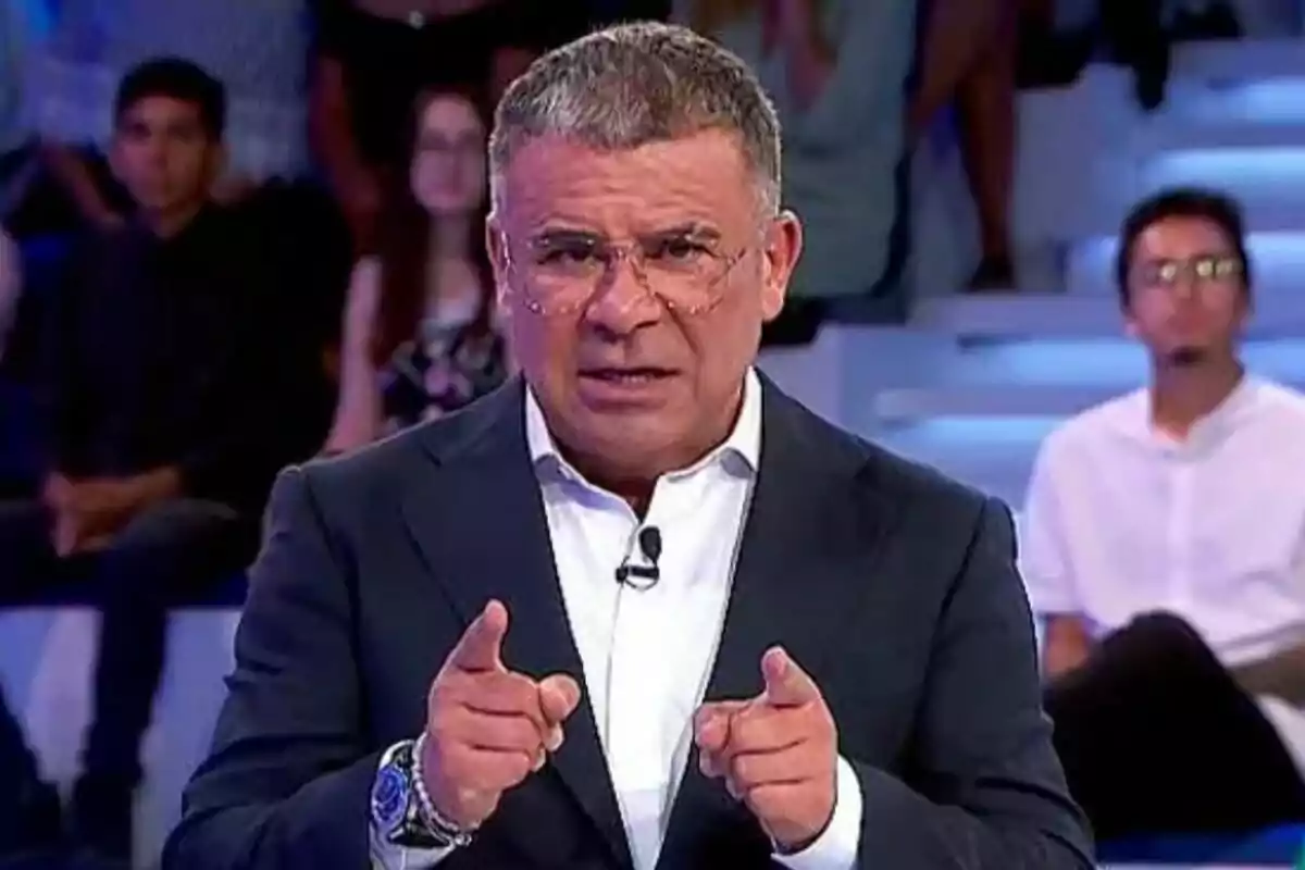 Jorge Javier Vázquez con gafas y traje oscuro gesticula con las manos en Hay una cosa que te quiero decir con personas sentadas al fondo.