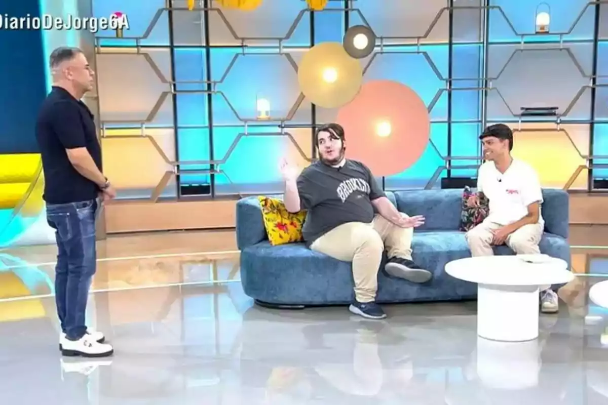 Captura de Jorge Javier Vázquez junto a varios invitados en El Diario de Jorge, dos sentadas en un sofá azul y una de pie frente a ellas, con un fondo colorido y moderno. Captura de Jorge Javier Vázquez junto a varios invitados en El Diario de Jorge, dos sentadas en un sofá azul y una de pie frente a ellas, con un fondo colorido y moderno.