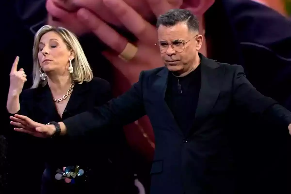 Dos personas en el plató de Gran Hermano, la madre de Violeta con gesto expresivo y Jorge Javier Vázquez con gafas y traje oscuro, ambos parecen estar en medio de una conversación tensa. Dos personas en el plató de Gran Hermano, la madre de Violeta con gesto expresivo y Jorge Javier Vázquez con gafas y traje oscuro, ambos parecen estar en medio de una conversación tensa.