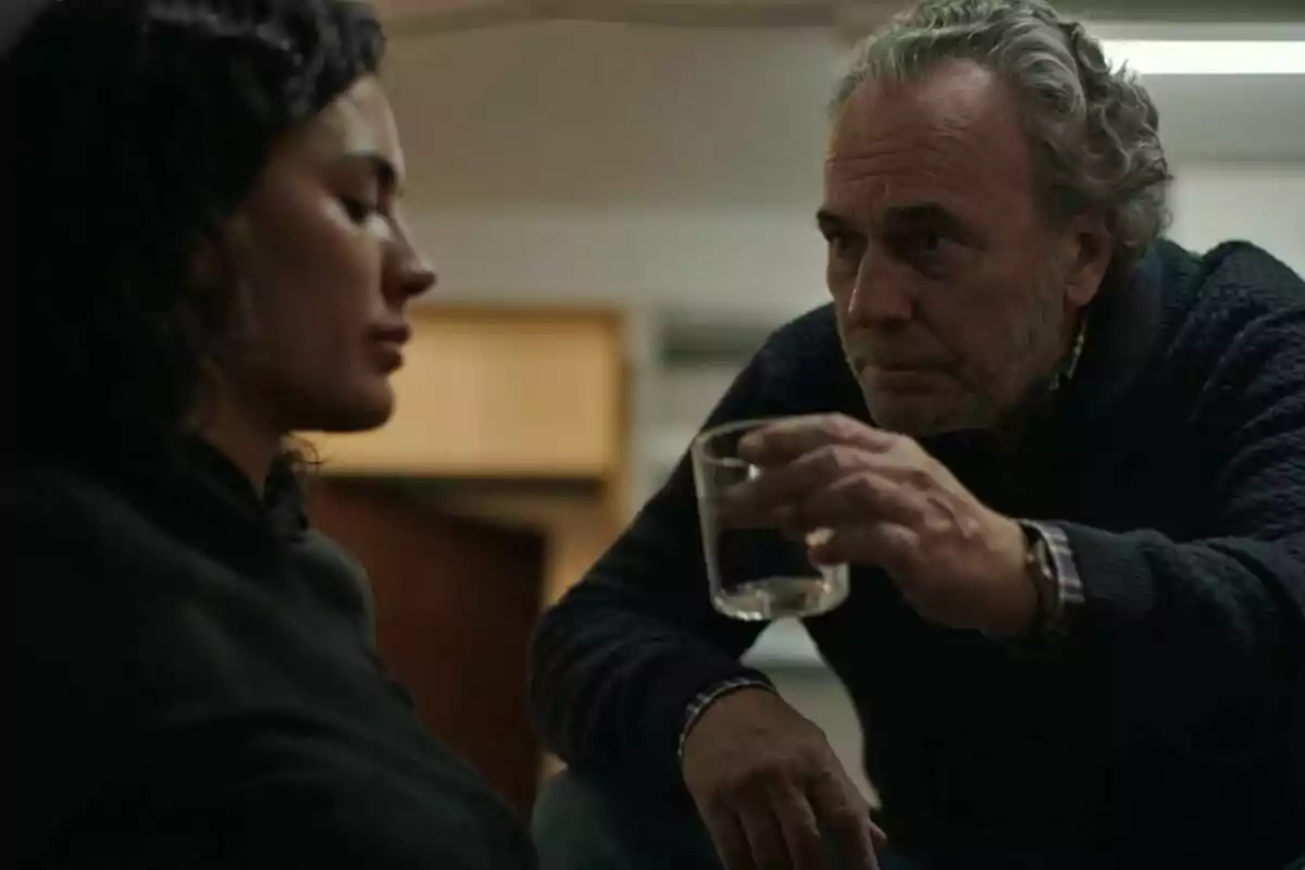 José Coronado ofrece un vaso de agua a Michelle Calvó que parece pensativa en un ambiente interior en Entrevías. José Coronado ofrece un vaso de agua a Michelle Calvó que parece pensativa en un ambiente interior en Entrevías.
