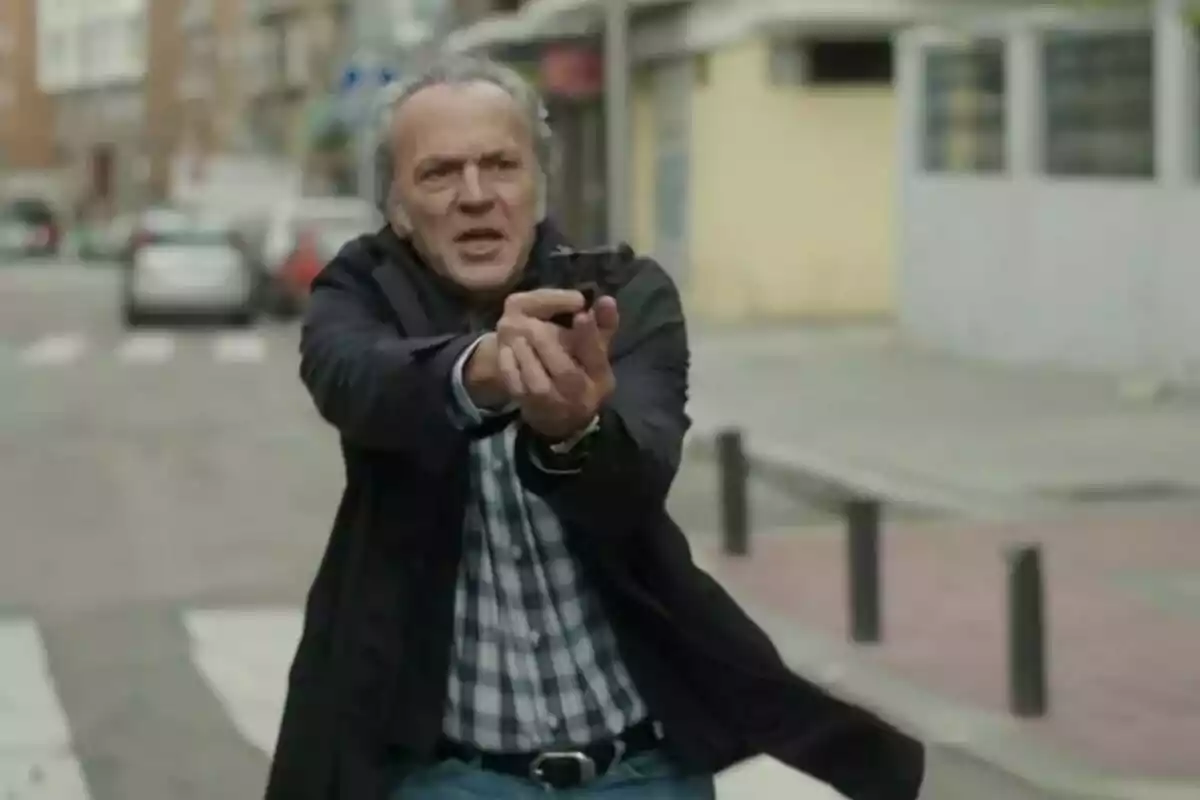 José Coronado amb cabell canós i jaqueta fosca apunta amb una pistola en un carrer urbà a la sèrie Entrevies José Coronado amb cabell canós i jaqueta fosca apunta amb una pistola en un carrer urbà a la sèrie Entrevies