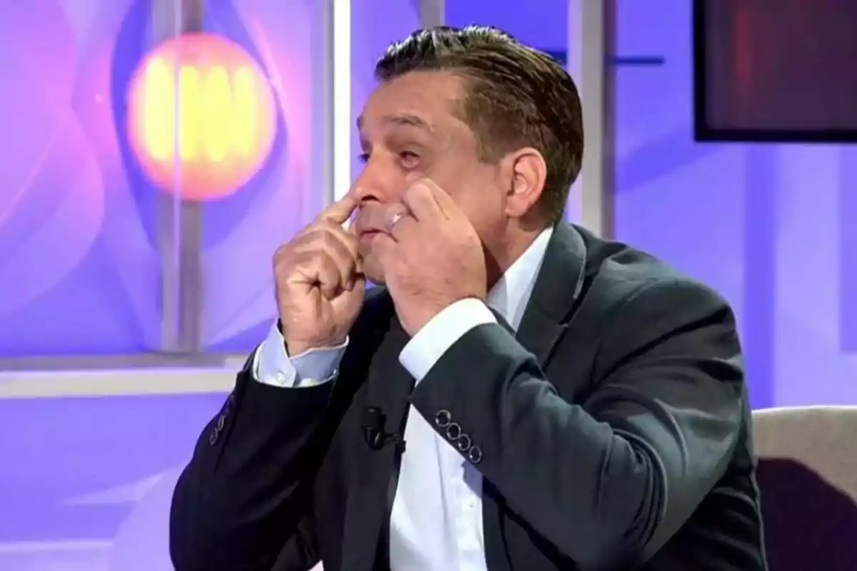 José Manuel Saborido en un estudio de televisión en Código 10 está señalando sus ojos con ambas manos mientras lleva puesto un traje oscuro.