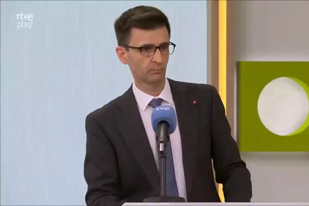 José Pablo López con gafas y traje oscuro habla frente a un micrófono azul en un estudio de televisión en la presentación de 2Cat. José Pablo López con gafas y traje oscuro habla frente a un micrófono azul en un estudio de televisión en la presentación de 2Cat.