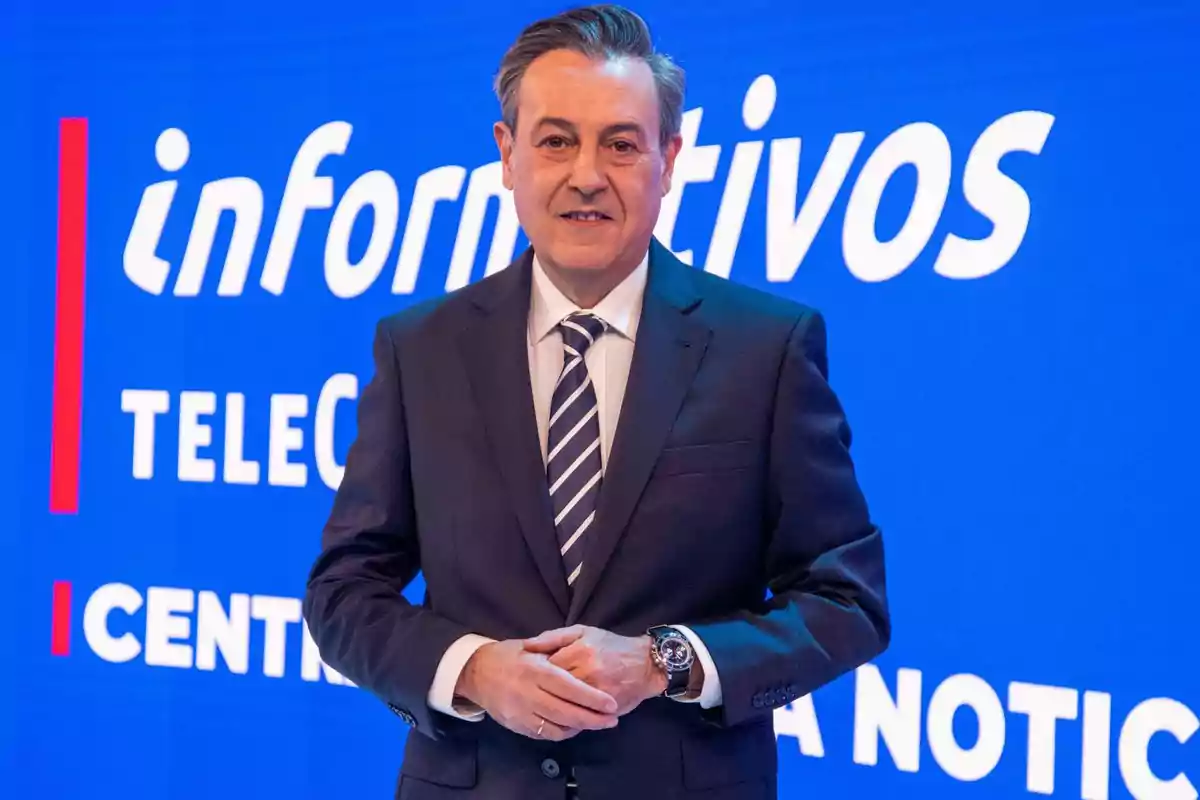 José Ribagorda con traje y corbata de pie frente a un fondo azul con el texto José Ribagorda con traje y corbata de pie frente a un fondo azul con el texto