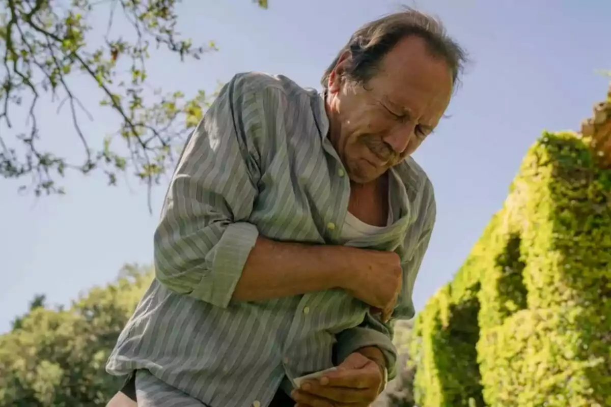 Juan Gea amb expressió de dolor subjectant-se el pit en un jardí assolellat a Sueños de Libertad. Juan Gea amb expressió de dolor subjectant-se el pit en un jardí assolellat a Sueños de Libertad.