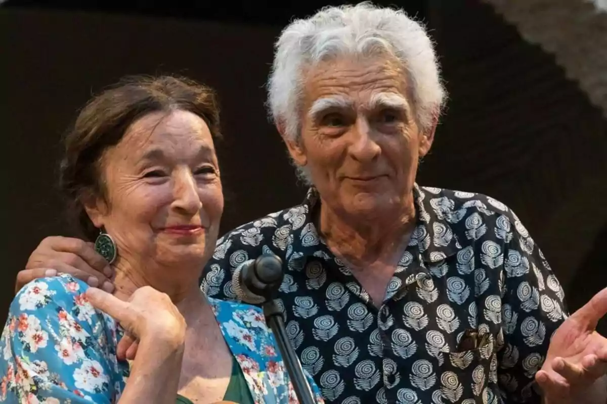 Petra Martínez i Juan Margallo grans somriuen mentre estan drets junts davant d'un micròfon.