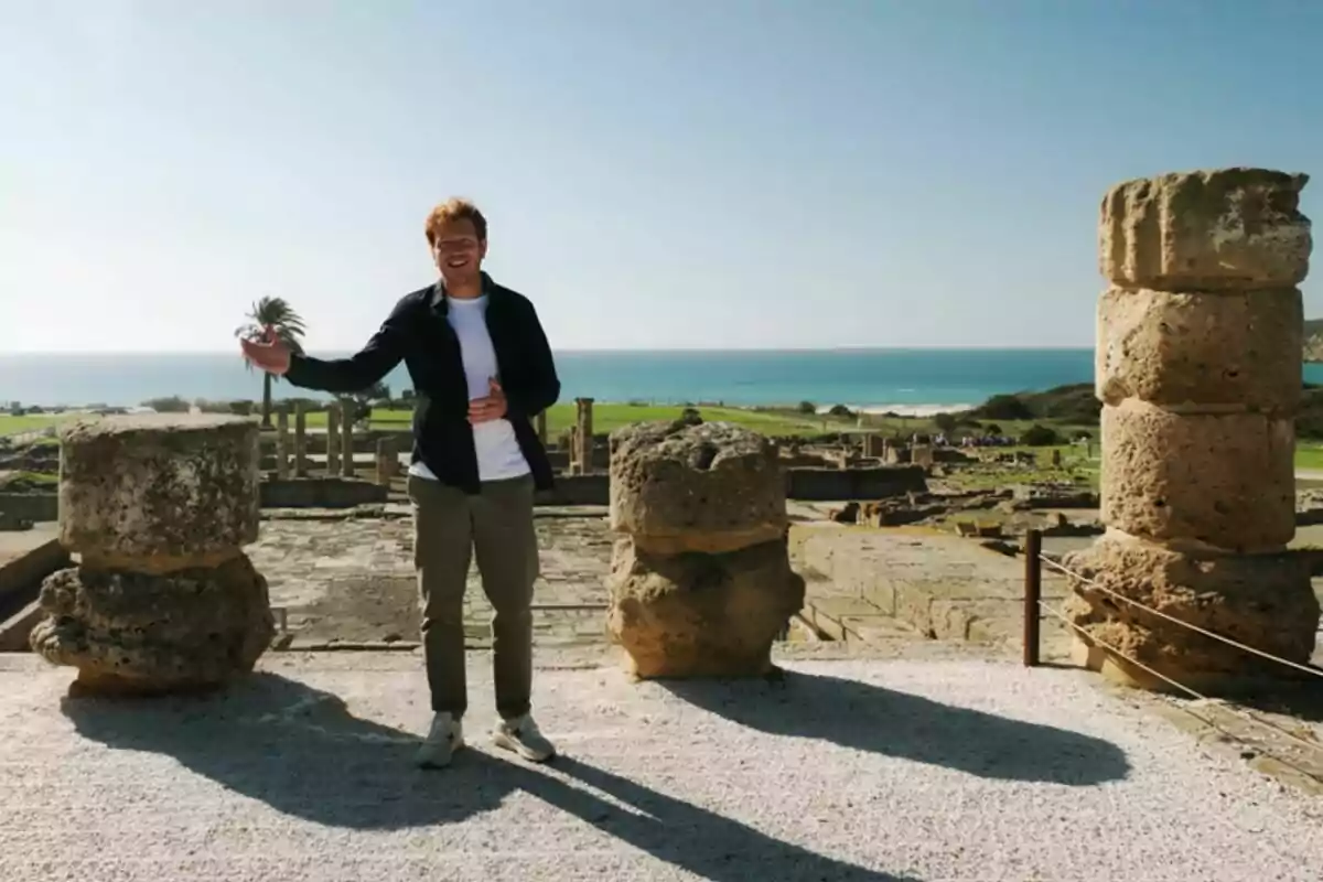 Juanlu González dret en un lloc arqueològic amb columnes antigues i el mar al fons en un dia assolellat a Desmuntant Andalusia. Juanlu González dret en un lloc arqueològic amb columnes antigues i el mar al fons en un dia assolellat a Desmuntant Andalusia.